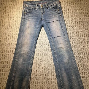 Blå jeans med broderade bakfickor - Snygga blå jeans med unika broderade detaljer på bakfickorna. Trådarna på framsidan är designen (jeansen har inte gått sönder). De är bootcut. Midja rakt över: 36cm. Lår: 26cm. Innerben: 85cm