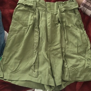 Gröna shorts från Beloved - Snygga gröna shorts från Beloved med hög midja och knytband. Perfekta för sommardagar med en avslappnad passform. Inkluderar extra knapp.