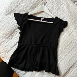 Svart ribbad topp - Snygg svart ribbad topp med korta ärmar och knytband i midjan. Perfekt för en stilren look.