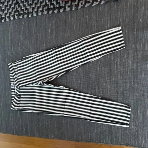 Randiga byxor från Vero Moda - Snygga svartvita randiga byxor från Vero Moda. Perfekta för en stilren look med en normal passform och midwaist. Byxorna har en klassisk design med dragkedja och knapp framtill.