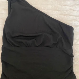 Svart oneshoulder topp - Snygg svart oneshoulder topp med ribbad textur. Perfekt för en stilren och modern look. Passar bra till både jeans och kjol.