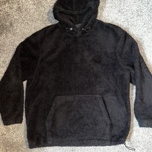 Svart fleece hoodie från H&M - Mysig svart hoodie i fleece från H&M med relaxed fit. Den har en stor ficka framtill och justerbar huva med dragsko. Perfekt för kyliga dagar.