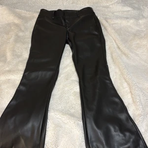 Svarta ”skinnbyxor”  - Snygga svarta skinnbyxor från Gina Tricot med hög midja och bootcut-stil. Perfekta för en trendig look med en tight passform upptill och utsvängda ben. Byxorna har en dragkedja och ”knappar” framtill, tyvärr inga fickor. Aldrig använt, råka ta sönder prislappen så fick inte lämna tillbaka dem. Stl 38.