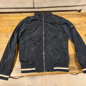 Marinblå/svart bomberjacka från Boss - Snygg marinblå bomberjacka från Boss med dragkedja, storlek L men passar M också. Den är oanvänd pågrund av att den var för stor på mig. Priset kan diskuteras vid en snabbaffär.