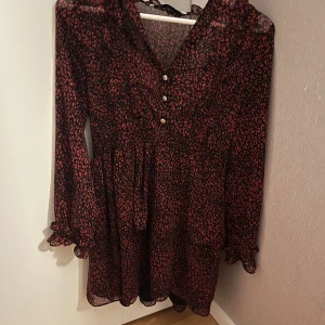 Svart och röd klänning från Zara - Snygg svart och röd klänning från Zara med ett leopardmönster. Klänningen har långa ärmar och knappar framtill. Perfekt för en trendig look. Använd 1 gång men inte mer än så!