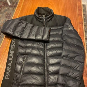 Parajunpers dunjacka  - Snygg svart dunjacka från Parajumpers med dragkedja och hög krage. Jackan har märkets logga på ärmen och är perfekt för kyliga dagar. Den quiltade designen ger både stil och värme.