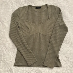 Beige ribbad tröja från KappAhl - Snygg beige ribbad tröja från KappAhl i storlek S. Tröjan har en unik skärning vid halsen och långa ärmar. Material är gjort på 77% polyester, 19% viskos och 1% elastan.