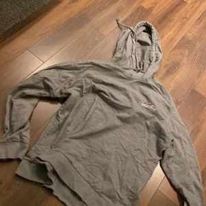 Grå hoodie från Jack & Jones - Säljer en grå hoodie från Jack & Jones. Den har en klassisk design med huva och dragsko samt långärmade ärmar. Perfekt för en avslappnad stil.