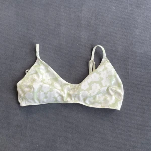 Blommig grön och vit bikini topp - Säljer en söt blommig bikini topp i grönt och vitt. Toppen har smala axelband och ett blommönster som ger en fräsch känsla. Perfekt för varma dagar!