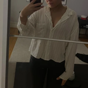 Vit och svart randig skjorta - Säljer en stilren vit skjorta med tunna svarta ränder. Skjortan har en avslappnad passform och långa ärmar, perfekt för en casual look. Den är tillverkad i ett lätt och bekvämt material. Storlek L men sitter som en s/m