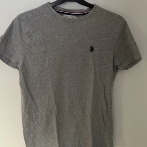 Grå t-shirt från U.S. Polo Assn. - Säljer en stilren grå t-shirt från U.S. Polo Assn. med en liten logga på bröstet. Perfekt för en avslappnad look. Gjord i mjukt material för extra komfort.