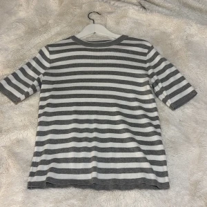 Grå- och vitrandig tröja - Säljer en stilren grå- och vitrandig tröja med korta ärmar. Tröjan har en rund halsringning och är tillverkad i ett mjukt material. Passar perfekt till ett par gråa byxor! 