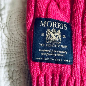 Röd kabelstickad tröja från Morris - Säljer en snygg röd kabelstickad tröja från Morris med v-ringning. Tröjan har långa ärmar, armbågslappar och ribbade muddar. Perfekt för att ge en färgklick till din garderob!