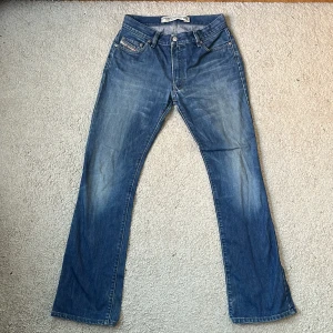 Blå jeans från Diesel - Snygga blå jeans från Diesel med klassisk femficksdesign och knappgylf. De har en avslappnad passform och är perfekta för en casual look. Märkesdetaljer på bakfickan och framfickan ger en extra touch. Sitter som W30 L32