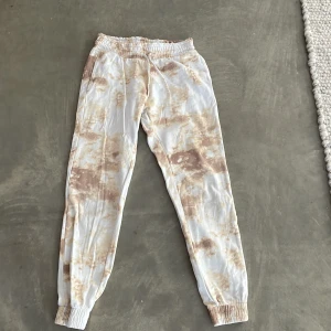 Mönstrade mjukisbyxor från Lindex - Säljer ett par bekväma mjukisbyxor från Lindex i storlek 146/152 för barn. Byxorna har ett unikt mönster i beige och vit med elastisk midja och muddar vid bensluten. Perfekta för en avslappnad dag hemma. Dem har ett litet hå på baksidan som ni ser på bilderna men annars i toppen skick❤️