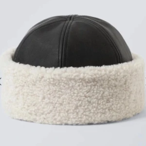 Svart skinnmössa med vit päls - Snygg svart mössa i skinn med mjuk vit pälsdetalj runt kanten. Perfekt för kalla dagar när du vill hålla dig varm och stilren.