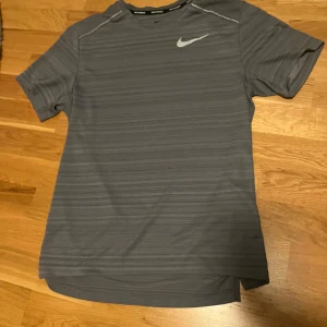 Grå Dri-FIT t-shirt från Nike storlek S - Säljer en grå Dri-FIT t-shirt från Nike med diskret randigt mönster. Perfekt för löpning och träning. Kortärmad design med Nike-logga på bröstet. Storlek S.
