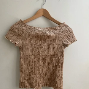 Guldig offshoulder topp med glittriga detaljer - Snygg guldig offshoulder topp med glittriga detaljer. Den har en ribbad struktur och korta ärmar, perfekt för en trendig look.