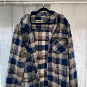 Blå och vit rutig overshirt från Woodbird - Säljer en snygg blå och vit rutig overshirt från Woodbird. Den har långa ärmar och knappar framtill. Perfekt för lager-på-lager-stil och ger en avslappnad look.