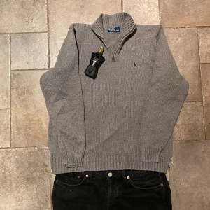 Ralph Lauren Quarter Zip Large - Säljer en stilren grå stickad Quarter Zip från Polo Ralph Lauren. Tröjan har ett diskret broderat logotypmärke på bröstet och ribbade muddar vid ärmslut och nederkant. Perfekt för kyligare dagar! Riktigt fint skick och i storlek Large.