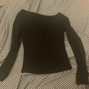 Svart långärmad topp - Snygg svart långärmad topp med offshoulder-design. Perfekt för en stilren look. Tillverkad i ett mjukt och stretchigt material som ger en bekväm passform.