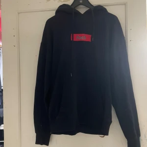 Svart hoodie från ESBN - Säljer en svart hoodie från ESBN med en röd och vit textdetalj på bröstet. Hoodien har en klassisk design med dragsko i huvan och ribbade muddar vid ärmslut och nederkant. Perfekt för en avslappnad stil.