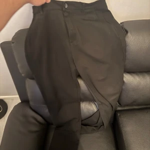 Svarta kostymbyxor från pondus - Snygga svarta kostymbyxor med knappar och dragkedja. Perfekta för en stilren look. Passar bra till både formella och avslappnade tillfällen. En knapp fattas men det synns inte!