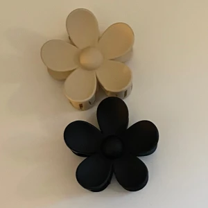 Blomformade hårklämmor - Två blommformade hårklämmor, en i svart och en i beige. 10 kr/styck eller 15 kr för båda! Hör av er vid frågor💕