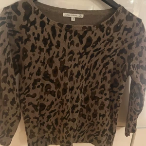 Leopardmönstrad tröja från Flash Essential - Snygg leopardmönstrad tröja från Flash Essential i beige och svart. Tröjan har trekvartsärmar och en rund halsringning. Perfekt för att ge din outfit en trendig touch.