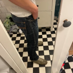 Mörkblå Nudie jeans - Mörk blå Nudie jeans i mycket bra skick men slitningar vid benöppningens baksida (bild 4&5). Faller RIKTIGT SNYGGT på skor, men säljer eftersom jag tycker de är för liten midja storlek för mig. Modell: Low Slim Jim