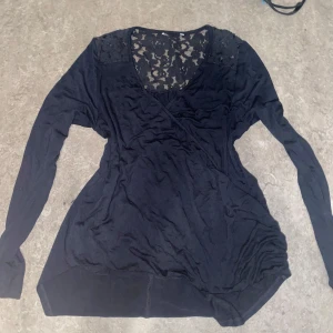 Svart långärmad topp med spetsdetaljer - Snygg svart långärmad topp med spetsdetaljer vid axlarna och en v-ringad design. Perfekt för en stilren look.