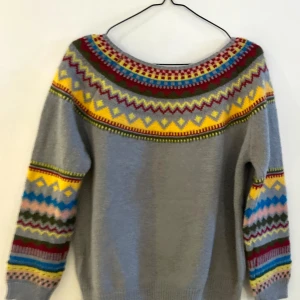 Grå stickad tröja med färgglatt mönster - Säljer en mysig grå stickad tröja med ett färgglatt mönster i gult, rött, turkosblått och grönt. Tröjan har långa ärmar och ett detaljerat mönster runt halsen och ärmsluten. Perfekt för kyliga dagar! Helt oanvänd. Storleken är L men är liten i storleken. Mer för någon med strl S eller M. 