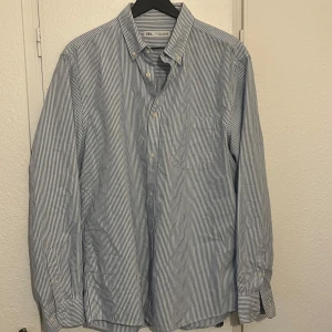 Randig skjorta från Zara - Snygg blå- och vitrandig skjorta från Zara med klassisk krage och knappar framtill. Fint skick,  använd fåtal gånger.