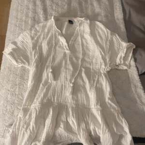 Vit klänning från Gina Tricot - Säljer en luftig vit klänning från Gina Tricot i storlek XS. Klänningen har korta ärmar och en v-ringad design med knytband. Perfekt för varma dagar!