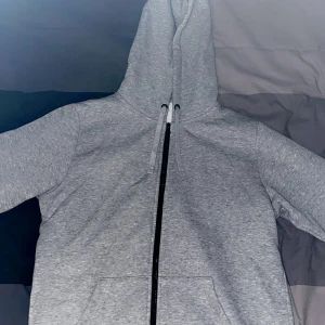 Grå hoodie med dragkedja - Säljer en klassisk grå hoodie med dragkedja och huva. Perfekt för en avslappnad stil. Den har långa ärmar och en bekväm passform.