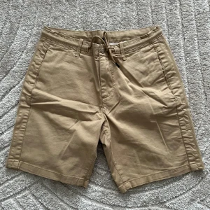 Beige shorts med snörning - Snygga beige shorts med praktisk snörning i midjan och knappstängning. Perfekta för en avslappnad stil. Två fickor fram och två bakfickor med knappar. PERFEKT FÖR dig som behöver något lite extra för speciella träff där du behöver något mer moget och klassikt