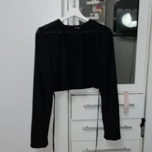 Svart croppad topp från NA-KD - Säljer en stilren svart croppad topp från NA-KD. Toppen har långa ärmar och en enkel design som passar perfekt till olika outfits. Perfekt för en trendig look! Är även en tunn topp