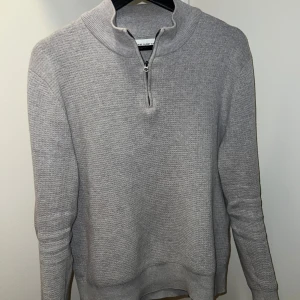 Grå halvzip från These Glory Days - Snygg grå stickad tröja från These Glory Days med dragkedja vid halsen. Perfekt för kyligare dagar med sin mjuka och bekväma passform. Tröjan har långa ärmar och en stilren design.