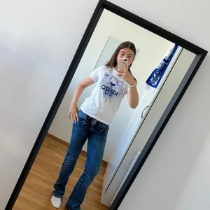 Vit t-shirt från Kenzo - Säljer en snygg vit t-shirt från Kenzo med ett coolt tigertryck i blått och texten 'Kenzo Paris' på framsidan. T-shirten är i bra skick och passar perfekt till vardags eller fest. Den är gjord av bomull och har en normal passform. Perfekt för dig som vill ha något stilrent men ändå med en twist!