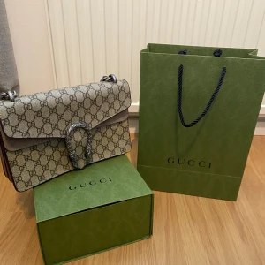 Gucci Dionysus Axelväska - Beige - Gucci Dionysus axelväska i färgen beige. Ikonisk tigerdetalj och kedjerem för en perfekt look. Perfekt storlek för mobil, plånbok och smink. Mycket fint skick, lyxig och tidlös design. Missa inte chansen att äga denna! Kontakta mig vid intresse.