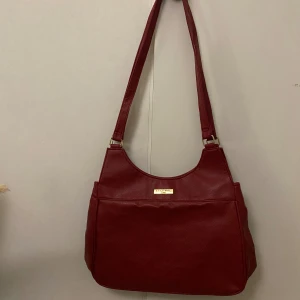 Väska - Vinröd väska köpt second hand. Finns två fack inuti väskan och ett på baksidan. Vet inte vad det är för märke men den är i ett bra skick. 