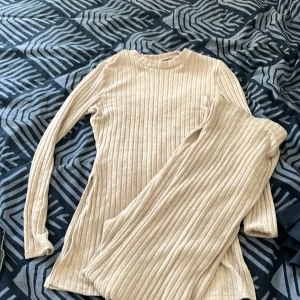 Beige ribbad byxdress - Säljer en superfin beige ribbad byxdress. Den är gjord av ett mjukt och stretchigt material som känns skönt mot huden. Byxdressen har långa ärmar och vida byxben, vilket ger en avslappnad och stilren look. Perfekt för både vardag och fest!