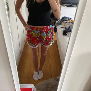 Säljer ett par superfina röda shorts med blommigt mönster och spetsdetaljer längst ner. Perfekta för sommaren! De är bekväma och har en lös passform. Passar perfekt till stranden eller en varm sommardag. 🏖️🌸köpta på marknad i Frankrike så vet därför inte märket.