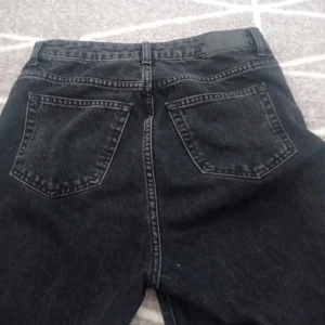 Svarta jeansbyxor - Byxorna har en klassisk femficksdesign med en knapp och dragkedja framtill. De är tillverkade i ett slitstarkt jeanstyg och har en rå kant vid bensluten för en cool, avslappnad look. Perfekta för vardags+ ger ett par grattis smycken 