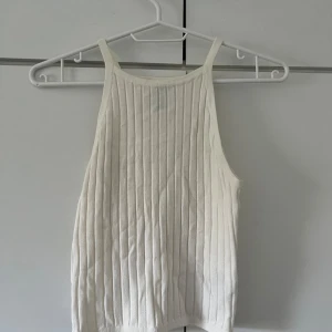 Vit ribbad linnetopp - Säljer en snygg vit ribbad linnetopp. Den är ärmlös och har en tight passform, perfekt för sommaren. Materialet är mjukt och stretchigt, vilket gör den bekväm att bära hela dagen. Passar både till vardags och festliga tillfällen.