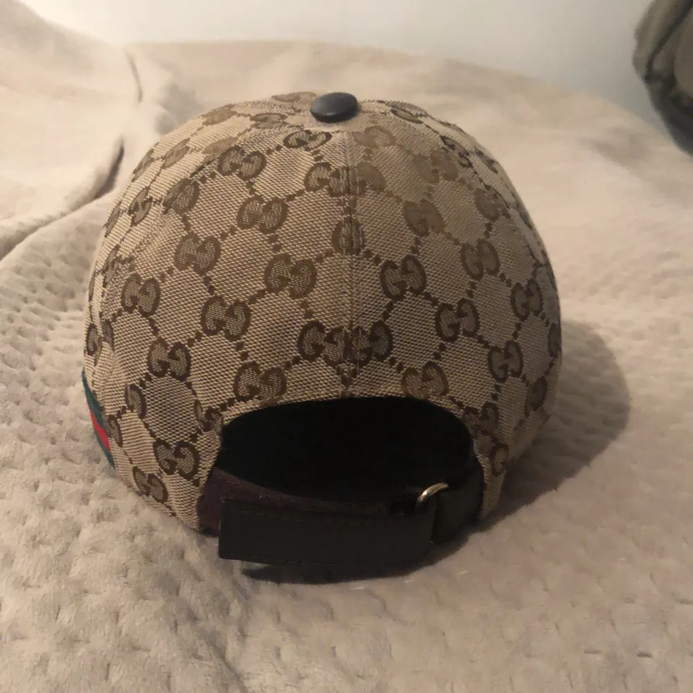 Säljer en snygg beige keps från Gucci med deras ikoniska GG-mönster. Kepsen är i storlek XS (56 cm) och har en justerbar rem baktill för perfekt passform. Perfekt accessoar för att lyfta din outfit!. Accessoarer.