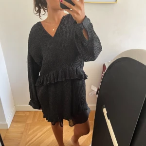 Svart glittrig klänning - Säljer en superfin svart prickig klänning med volangdetaljer. Klänningen har en v-ringad hals och långa ärmar. Perfekt för fest eller nyår! 🖤✨