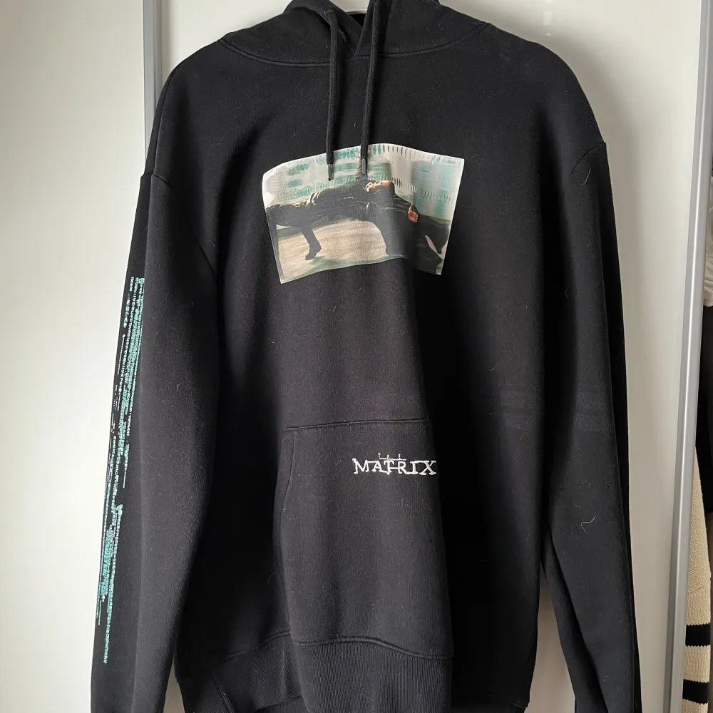 Säljer en svart hoodie från H&M med Matrix-tryck på framsidan och tryck längs ena ärmen. Den är i storlek XL men sitter som L . Neuletakit & Villapaidat.