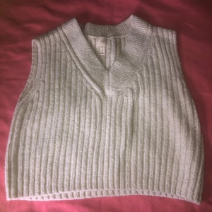 Beige stickad väst - Säljer en superfin beige stickad väst i storlek M. Den är ribbad och har en snygg v-ringad design. Perfekt för höst och vinter, och kan stylas både till vardags och fest. Västen är i använd och väldigt bekväm att ha på sig. Passar perfekt över en skjorta eller långärmad tröja!