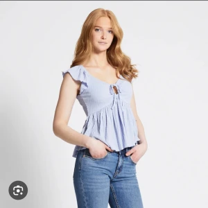 Ljusblå topp med volanger och knytning - Säljer en superfin ljusblå topp med volanger på ärmarna och en söt knytning framtill. Toppen är perfekt för sommaren och har en luftig och bekväm passform. Den är tillverkad i ett mjukt och skönt material som känns härligt mot huden. Passar både till vardags och fest!